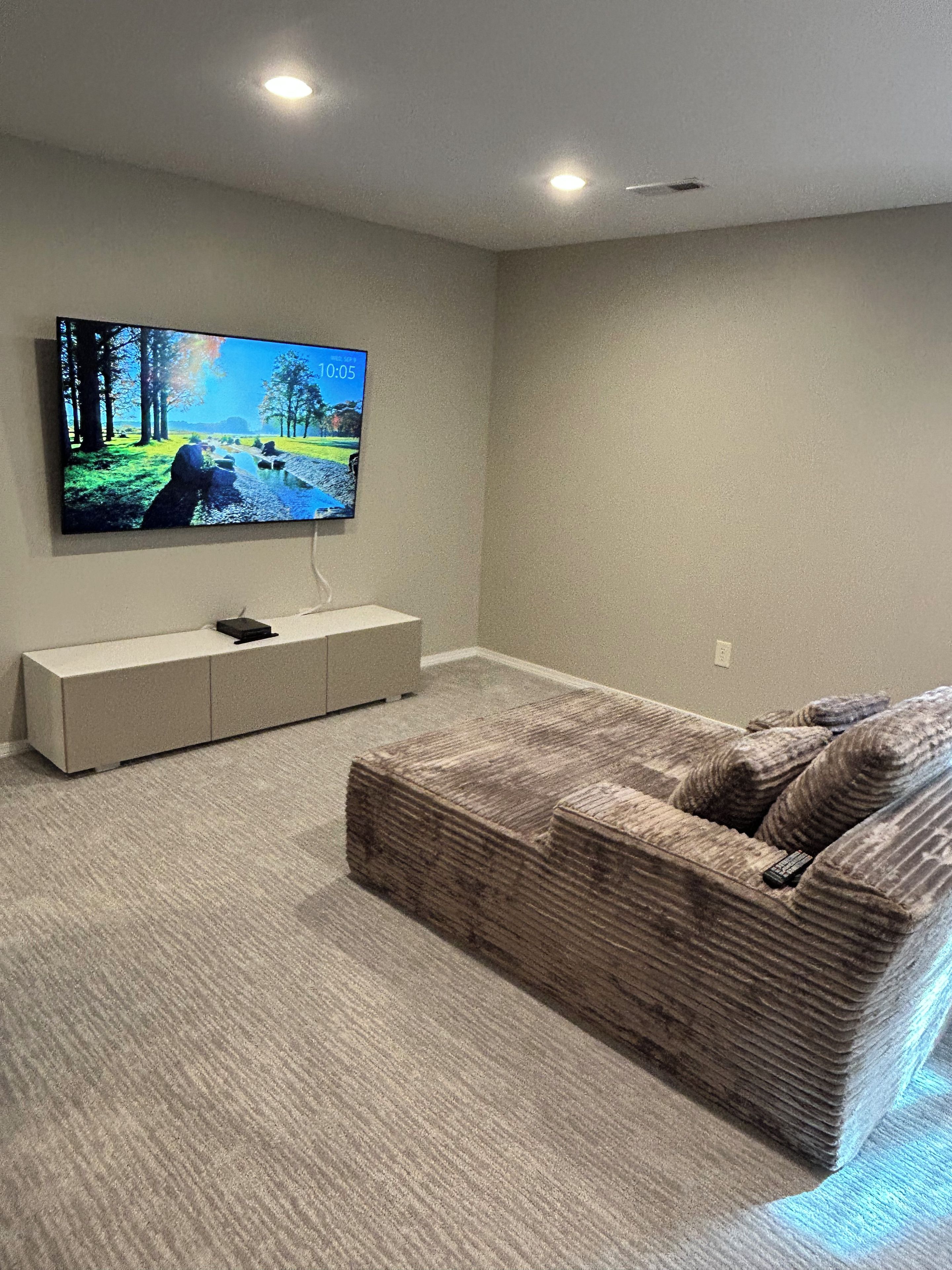 Een woonkamer met een flatscreen televisie aan de muur, een beige bank en een laag dressoir.