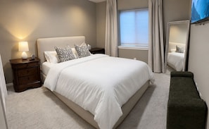 A neatly made bed with a white comforter and patterned pillows, a bedside lamp, a wooden nightstand, and a dark bench. - Cozy 3BR Escape in Wichita, Patio & Fire Pit (Wichita)