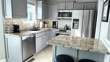 A modern kitchen with grey cabinets, stainless steel appliances, a granite countertop, and two bar stools.
