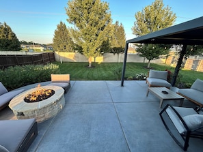 A patio with a stone fire pit, outdoor furniture, and a covered seating area.