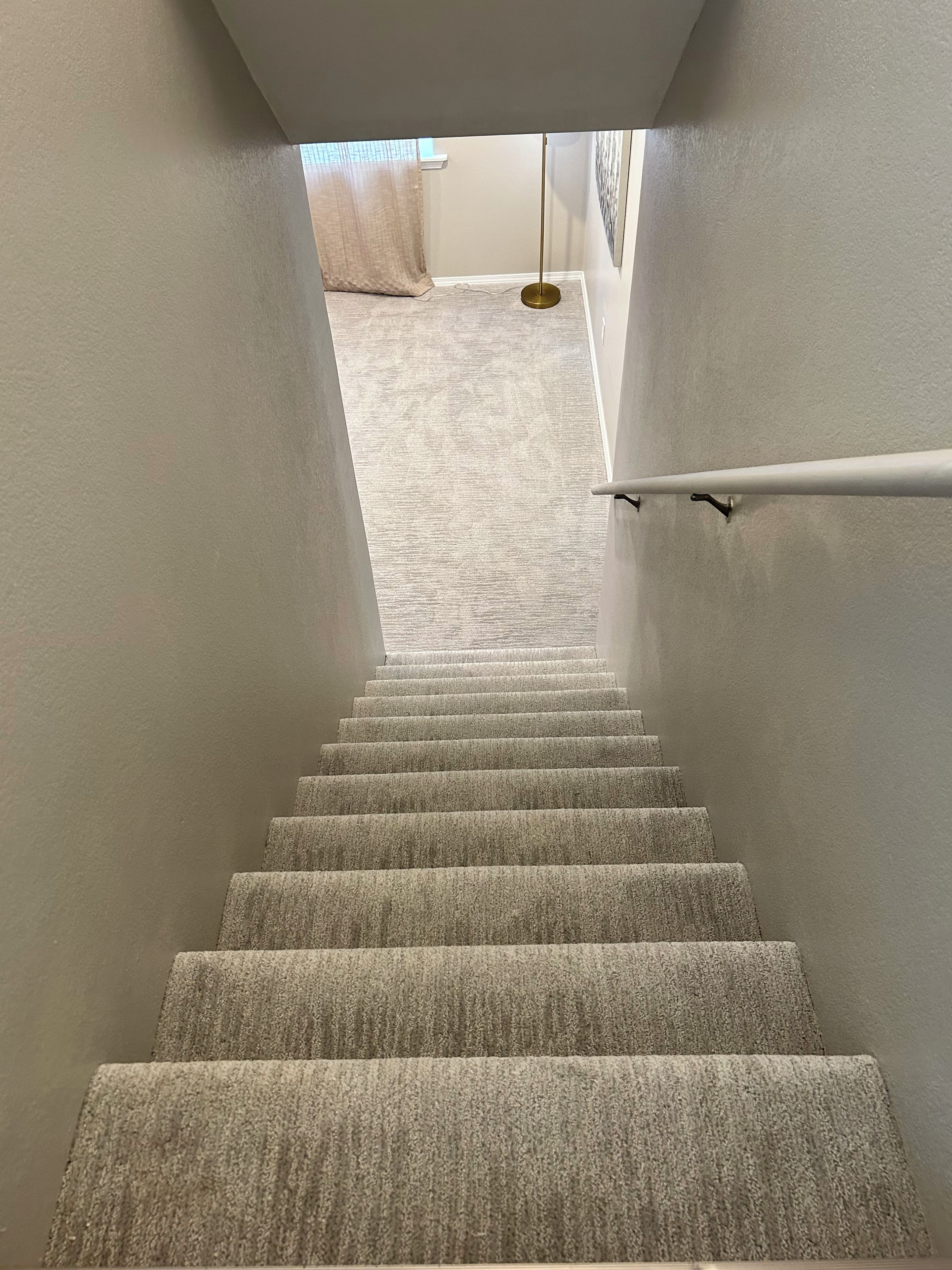 Una escalera alfombrada con barandilla que conduce a una habitación con ventana y una lámpara colgante.