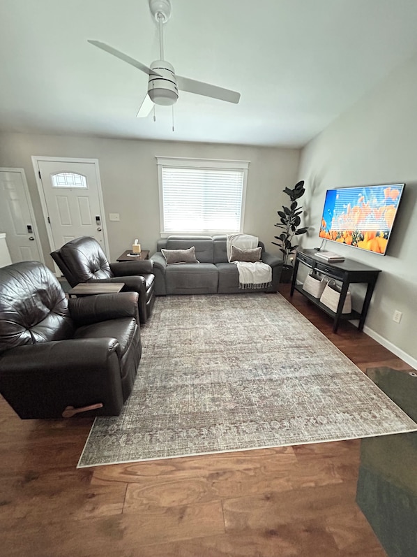 A living room with a grey sofa, black leather chairs, a grey rug, a television, and a ceiling fan. - Cozy 3BR Escape in Wichita, Patio & Fire Pit (Wichita)