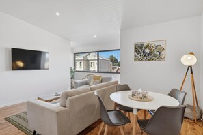A modern living room with a sofa, a coffee table, and a TV mounted on the wall. - Warwick 2 – Stylish Hobart Retreat (North Hobart)