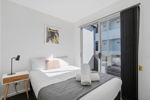 A hotel room with a bed, a desk, a lamp, a painting, and a view of the outside. - Warwick 2 – Stylish Hobart Retreat (North Hobart)