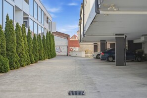 A parking garage with a row of parked cars, a concrete pathway, and a row of green trees on the left. - Warwick 2 – Stylish Hobart Retreat (North Hobart)