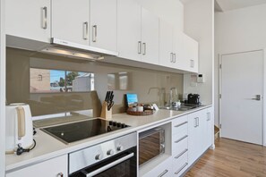 A modern kitchen with white cabinetry, a built-in oven, a stovetop, and a coffee machine. - Warwick 2 – Stylish Hobart Retreat (North Hobart)