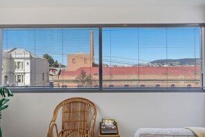A room with a large window overlooking a sports field and buildings. - Warwick 2 – Stylish Hobart Retreat (North Hobart)