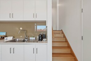A modern kitchen with white cabinets, a stainless steel sink, and a wooden staircase. - Warwick 2 – Stylish Hobart Retreat (North Hobart)