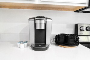 Eine Kaffeemaschine mit Wassertank, einer Kapselhalterung und einer schwarzen Kaffeekanne auf einer weißen Arbeitsplatte.