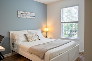 A bedroom with a bed, a nightstand, a lamp, a window, and a wall sign. - 3BR 2-Story House minutes from Downtown [Workspaces][FREE Level-2 EV Charging] (Raleigh)