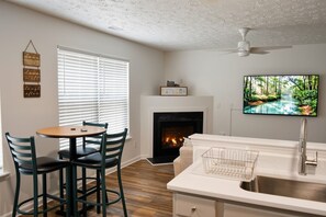 A living room with a fireplace, a television mounted on the wall, and a dining area with chairs and a table. - 3BR 2-Story House minutes from Downtown [Workspaces][FREE Level-2 EV Charging] (Raleigh)