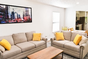Ein Wohnzimmer mit zwei Sofas, einem Couchtisch und einem Stadtbild an der Wand.
