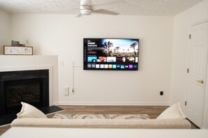 Ein Wohnzimmer mit Kamin, einem Wandfernseher, der eine Naturdokumentation zeigt, und einer Tür rechts.