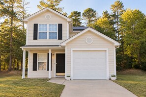 A two-story house with a garage, a front porch, and a well-maintained lawn. - 3BR 2-Story House minutes from Downtown [Workspaces][FREE Level-2 EV Charging] (Raleigh)