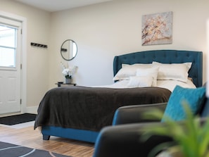 A bedroom with a bed, a bedside table, a mirror, and a painting on the wall.