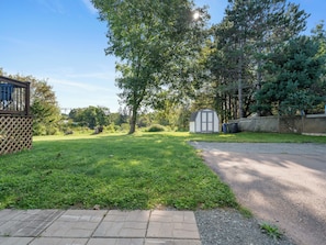 A grassy yard with a shed, a wooden fence, and a paved path. - Modern Two-Level Suite in Truro (Truro)