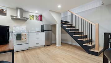 A modern kitchen with a built-in oven, a refrigerator, and a stove. There is a staircase with wooden steps and black railings.