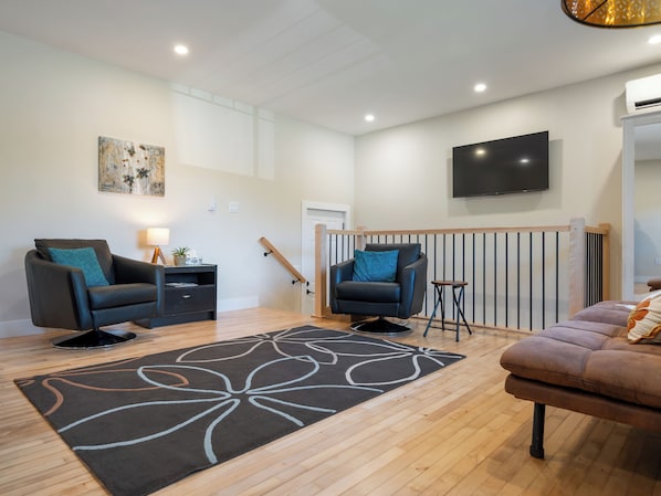 A modern living room with two sofas, a coffee table, a TV, and a staircase. - Modern Two-Level Suite in Truro (Truro)