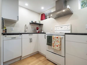 A compact kitchen with white cabinets, a dishwasher, a stove, and a sink. - Modern Two-Level Suite in Truro (Truro)