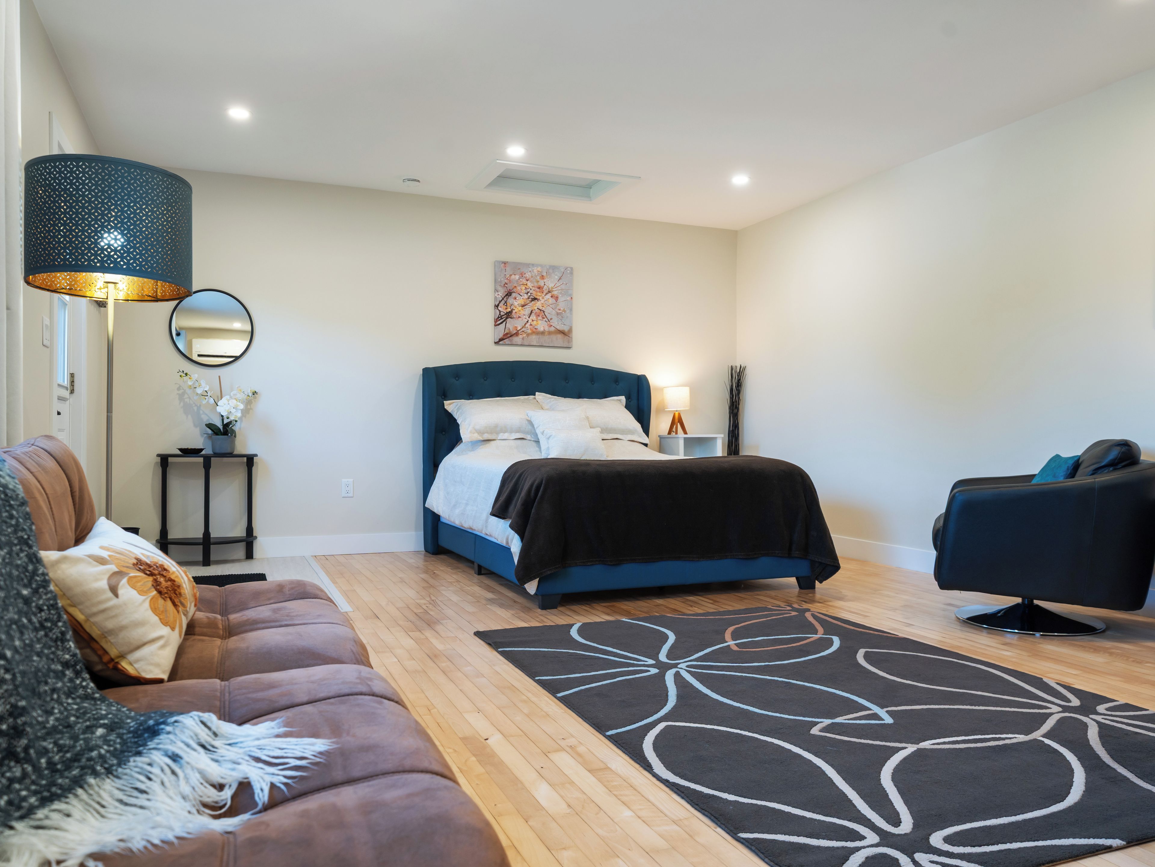 A bedroom with a bed, a nightstand, a lamp, a sofa, and a rug.
