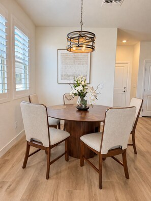 A dining area with a round wooden table, four upholstered chairs, a hanging light fixture, and a vase with white flowers. - Spacious 2-bedroom + office/gym townhome in charming Summerlin (Las Vegas)