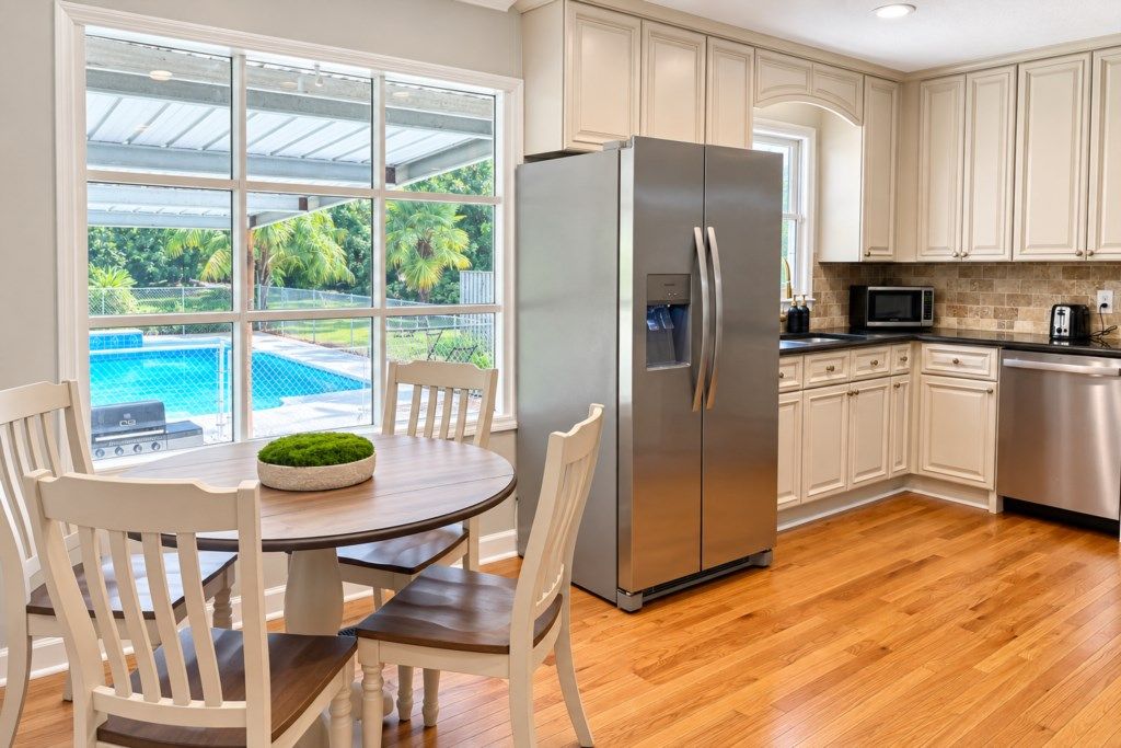 Eine moderne Küche mit einem Edelstahlkühlschrank, Holzboden und Blick auf einen Swimmingpool.