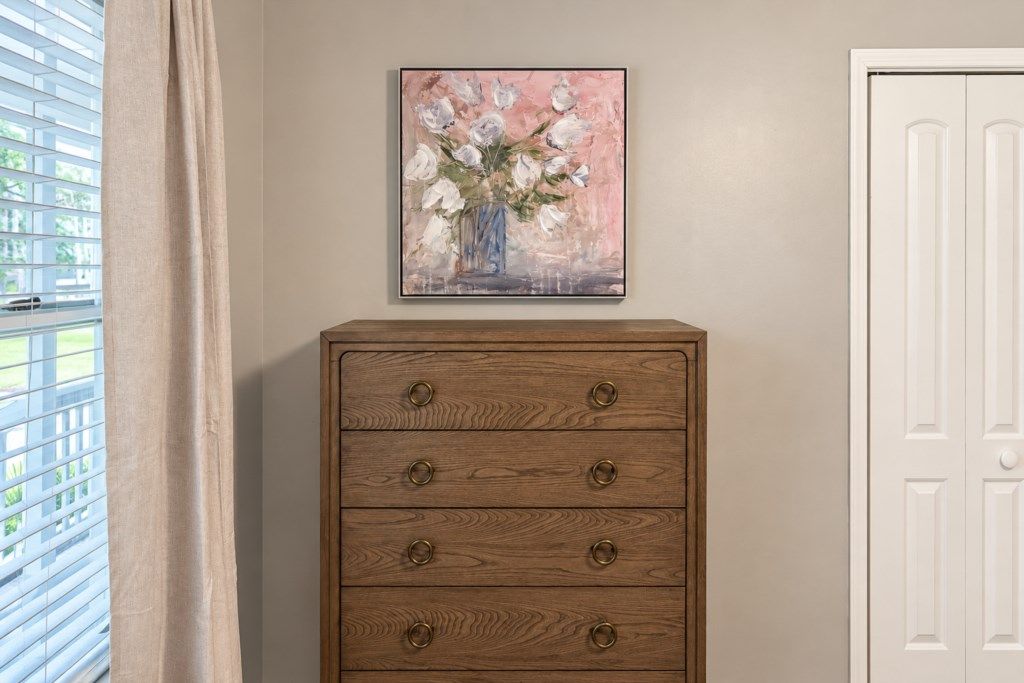 A wooden dresser with four drawers and a painting of flowers above it.