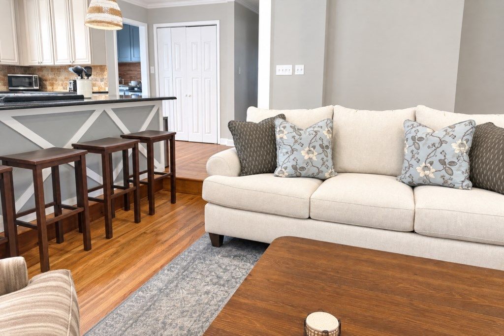A living room with a sofa, patterned cushions, a wooden coffee table, and a kitchen area in the background.