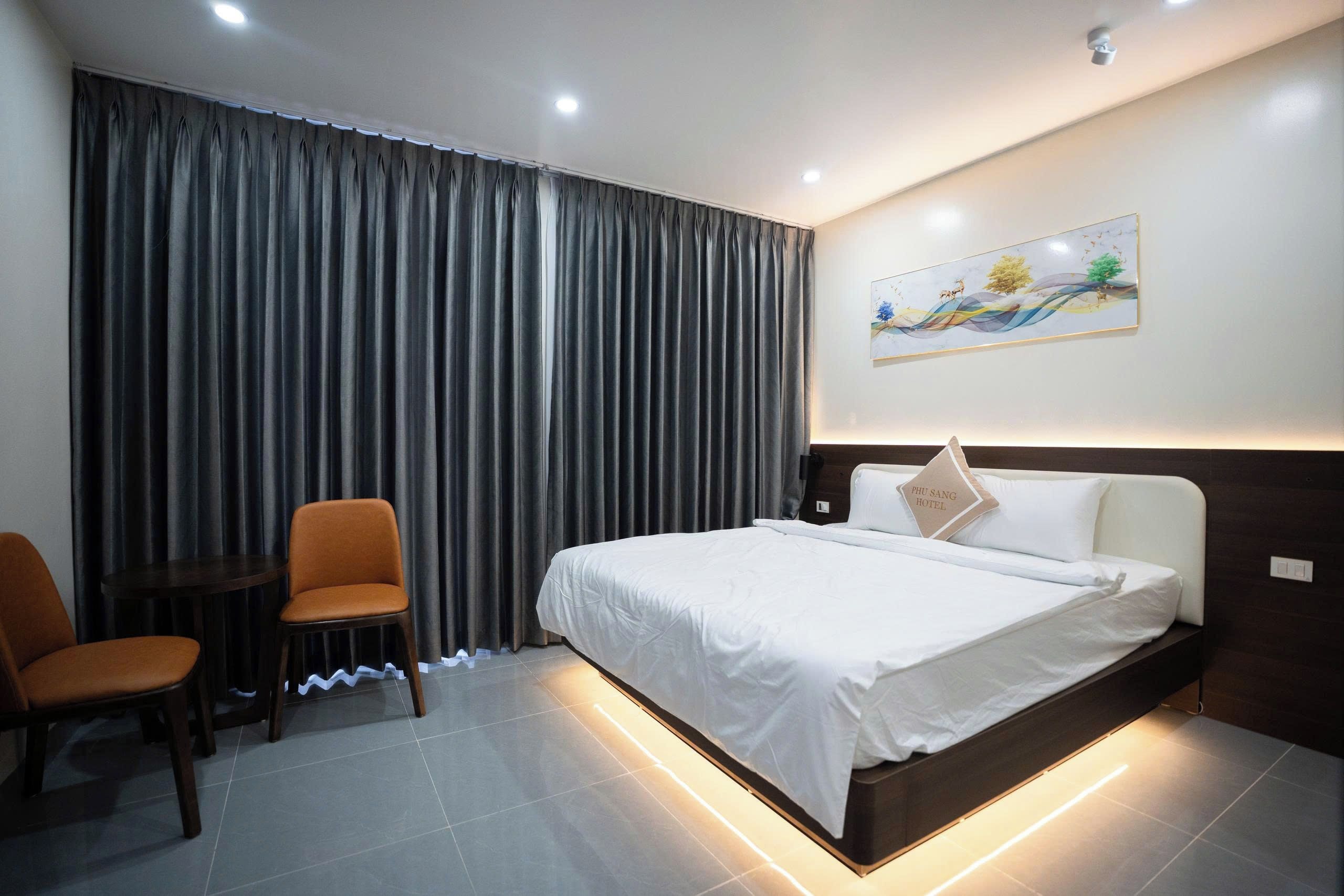 Una habitación de hotel con cama, una silla, una mesita y un cuadro en la pared.