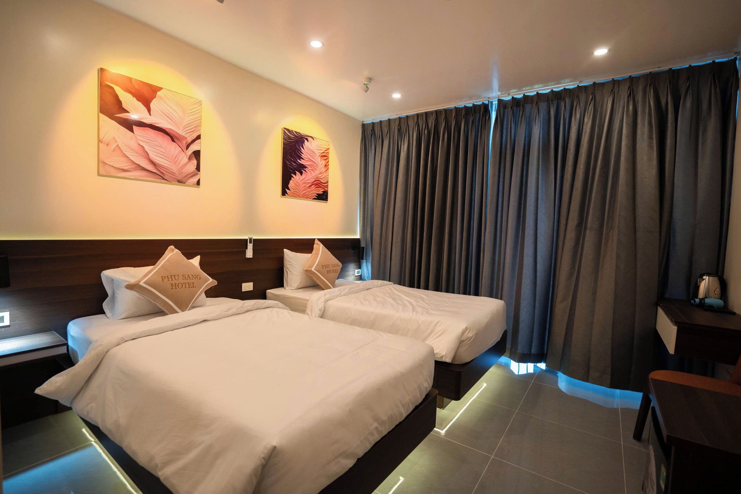 Habitació d'hotel amb dos llits, un escriptori i una finestra gran amb cortines.