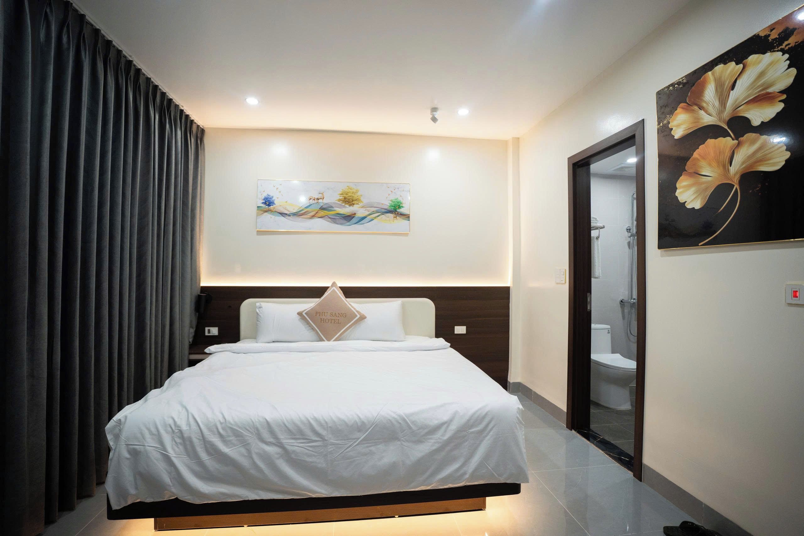 A hotel room with a bed, a painting on the wall, and a bathroom visible through an open door.