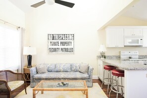 A living room with a sofa, coffee table, and a kitchen area with a microwave and stove.