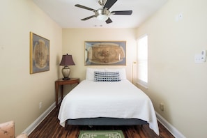A bedroom with a bed, a ceiling fan, a nightstand with a lamp, and two framed pictures on the wall.