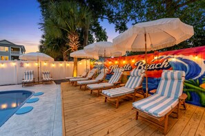A poolside area with lounge chairs and umbrellas, a wooden deck, and a mural with the words 'Little Beach'. - Beach Retreat-Sleeps 22-Outdoor Oasis-Golf Sim-Gym (North Myrtle Beach)