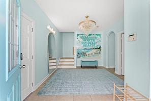 A hallway with a light blue wall, a wooden staircase, a blue rug, and a poster welcoming to North Myrtle Beach. - Beach Retreat-Sleeps 22-Outdoor Oasis-Golf Sim-Gym (North Myrtle Beach)