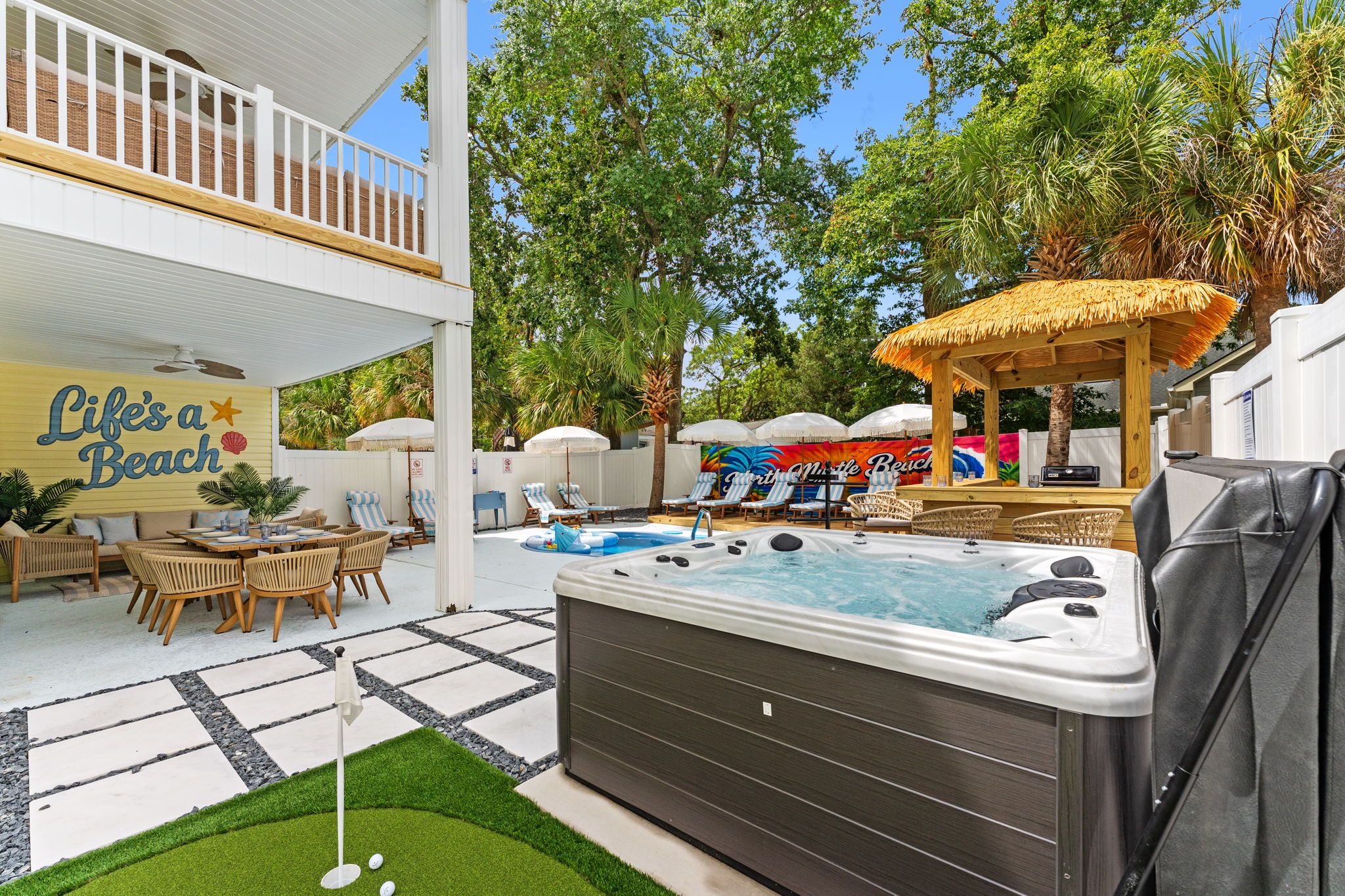 Ein Garten mit Whirlpool, Liegestühlen, einer überdachten Terrasse und einem Pool.