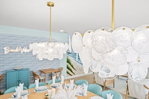 A dining area with a table set for four, a blue cabinet, and a wall with a beach-themed mural. - Beach Retreat-Sleeps 22-Outdoor Oasis-Golf Sim-Gym (North Myrtle Beach)
