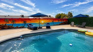Une piscine entourée de chaises longues et de parasols, le tout agrémenté d’une fresque murale aux couleurs vives.