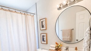 Une salle de bain avec un lavabo blanc, un miroir avec éclairage intégré, des toilettes et un rideau de douche.