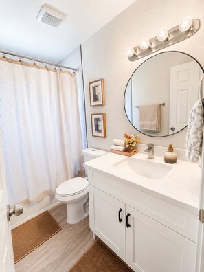 Een badkamer met een wit wastafel, een spiegel met verlichting, een toilet en een douchegordijn.