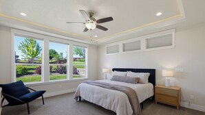 A bedroom with a bed, a chair, a nightstand, a ceiling fan, and large windows. - Spacious High End Ranch near Lake Lowell (Nampa)