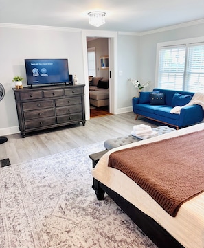 A bedroom with a bed, a dresser, a television, a blue sofa, and a window with blinds. - Historic charm meets contemporary style-steps away from downtown and waterfront (Washington)