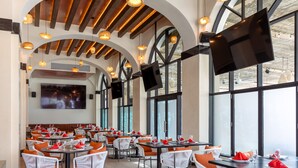 A restaurant with round tables, white chairs, and orange cushions. There are large windows and a TV mounted on the wall. - Luxury one bedroom suite located on an oceanfront resort in Cabo San Lucas (Cabo San Lucas)