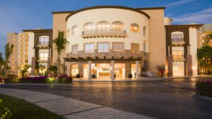 A multi-story hotel with a curved facade, large windows, and a central entrance with a covered walkway. - Luxury one bedroom suite located on an oceanfront resort in Cabo San Lucas (Cabo San Lucas)