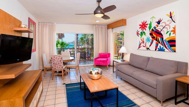 A modern living room with a flat-screen TV, a sofa, a dining table, and a colorful abstract painting. - Luxury one bedroom suite located on an oceanfront resort in Cabo San Lucas (Cabo San Lucas)