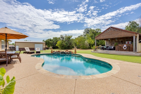 Ein Pool mit integriertem Wasserfall, umgeben von einer Terrasse mit Liegestühlen und einer überdachten Grillzone.