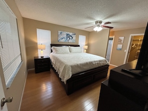 Une chambre à coucher avec un lit, des tables de chevet, un ventilateur de plafond et un téléviseur.