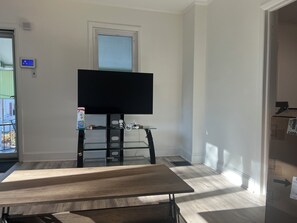 Una stanza con televisione su un mobile, una finestra, una porta e un tavolo.
