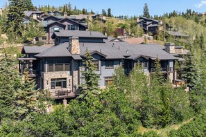 A large, multi-story house with a stone facade, multiple balconies, and a mountainous backdrop. - Exclusive Deer Valley 5BR | Hot Tub, Game Room, Views & Ski Shuttle (Park City)