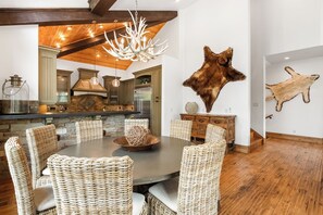 A dining area with a round table, wicker chairs, and a chandelier. - Exclusive Deer Valley 5BR | Hot Tub, Game Room, Views & Ski Shuttle (Park City)